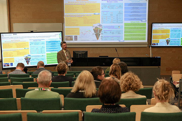 Na zdjęciu widać pana prezentującego wykład oraz salę w której siedzą słuchacze