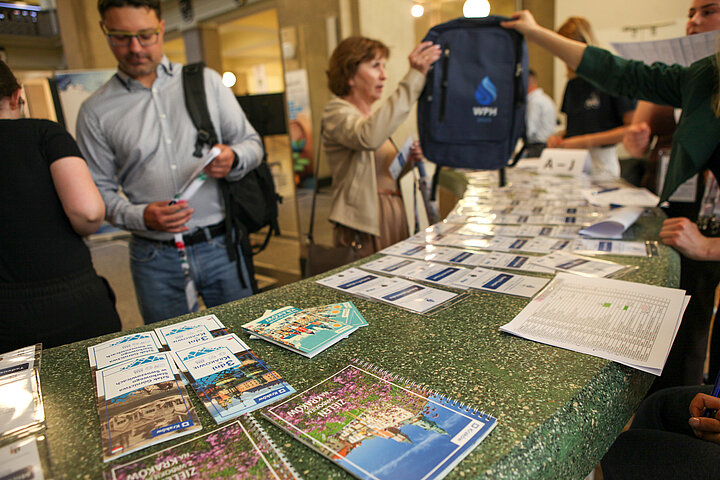 Na zdjęciu widać stanowisko rejestracji na konferencję oraz kilku uczestników, którzy się rejestrują