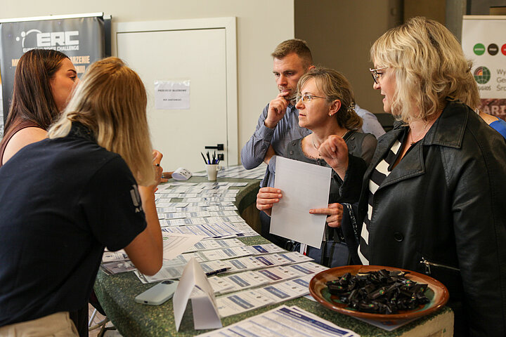 Na zdjęciu widać stanowisko rejestracji na konferencję oraz kilku uczestników, którzy się rejestrują