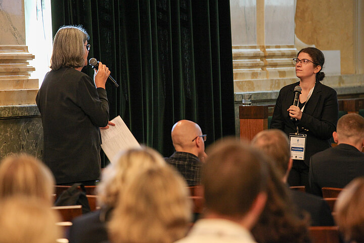 Na zdjęciu widać młodą studentkę przy mównicy odpowiadającą na pytanie z sali