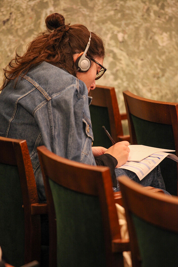 Na zdjęciu widać panią siedzącą w słuchawkach i notującą